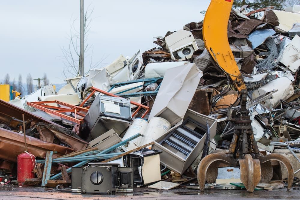 A Metal Claw Crane Scoops Up Scrap Metal and Appliances in a Junkyard — Central Scrap Metal in Ipswich, QLD
