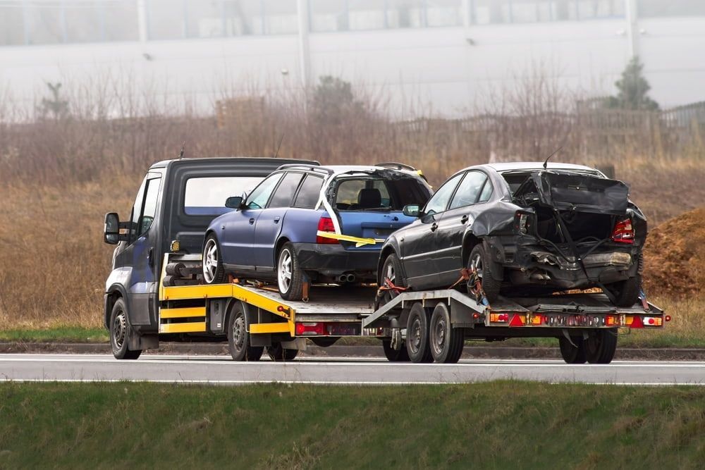 Tow Truck Carrying Two Severely Damaged Cars on a Roadway — Central Scrap Metal in Willawong, QLD