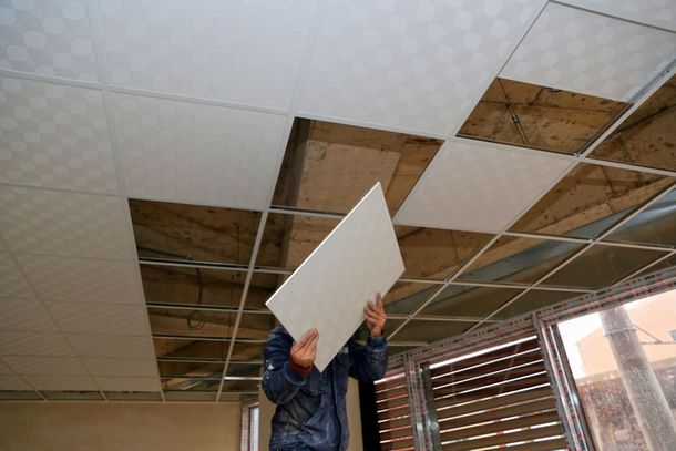 A man is holding a piece of tile up to the ceiling.