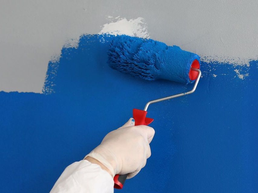 A person is painting a wall with a blue paint roller