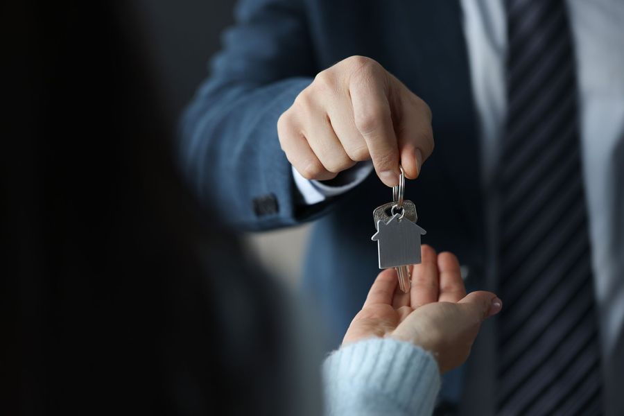 A man in a suit and tie is giving a woman a house key.