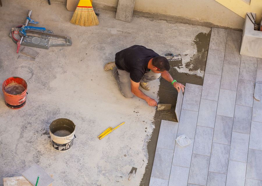 A man is laying tiles on a concrete floor.