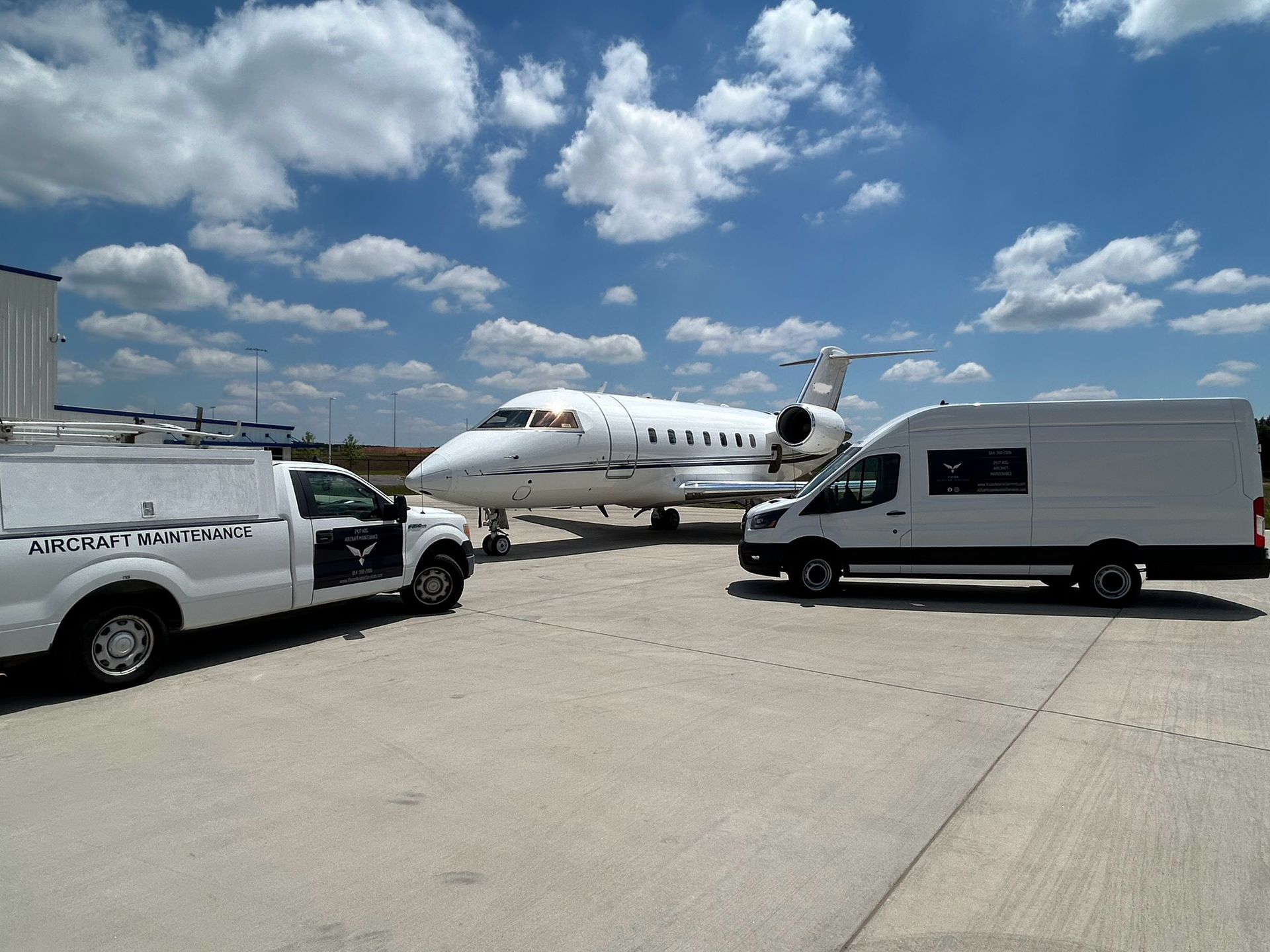 Two white vans are parked next to an airplane
