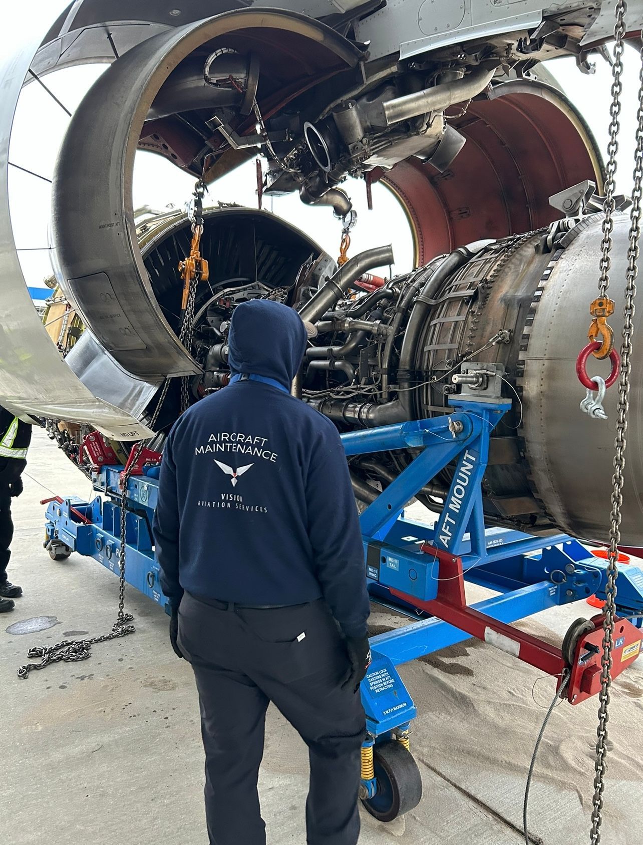 A man in a blue hoodie is standing in front of an airplane engine