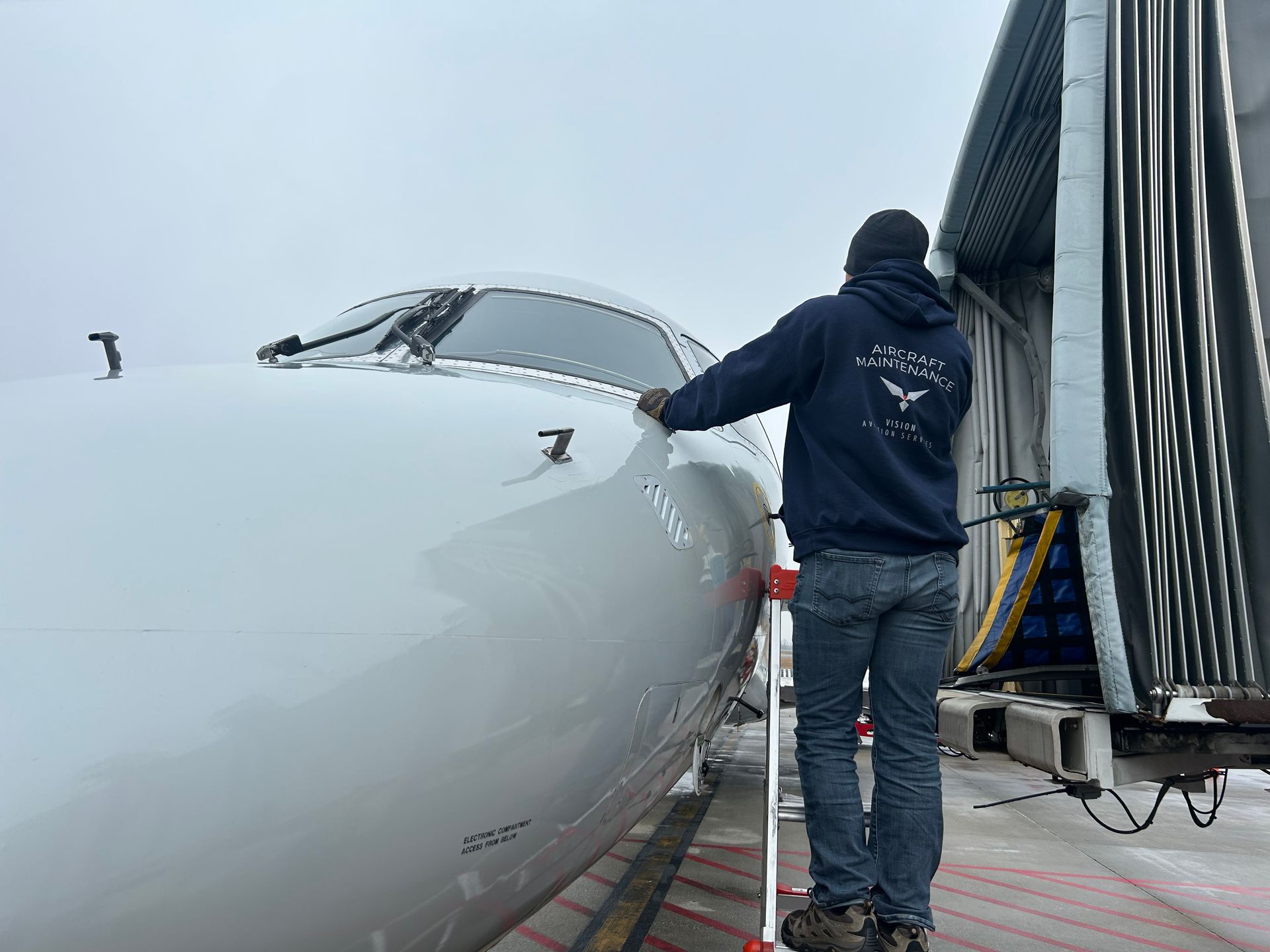A man in a blue hoodie is standing next to an airplane.