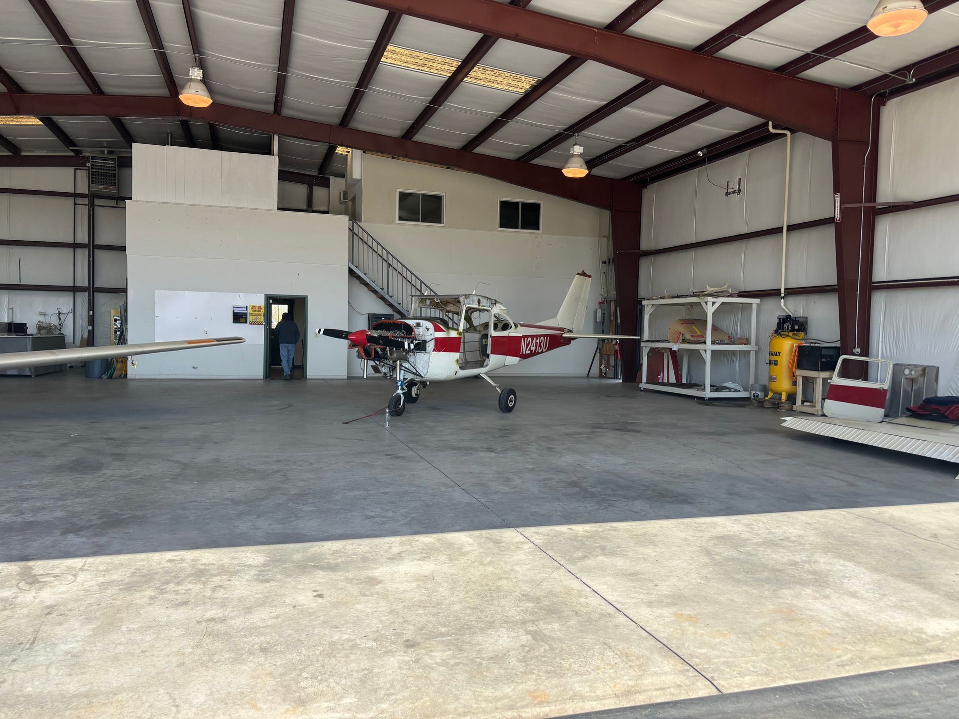 A small red and white plane is parked inside of a hangar.