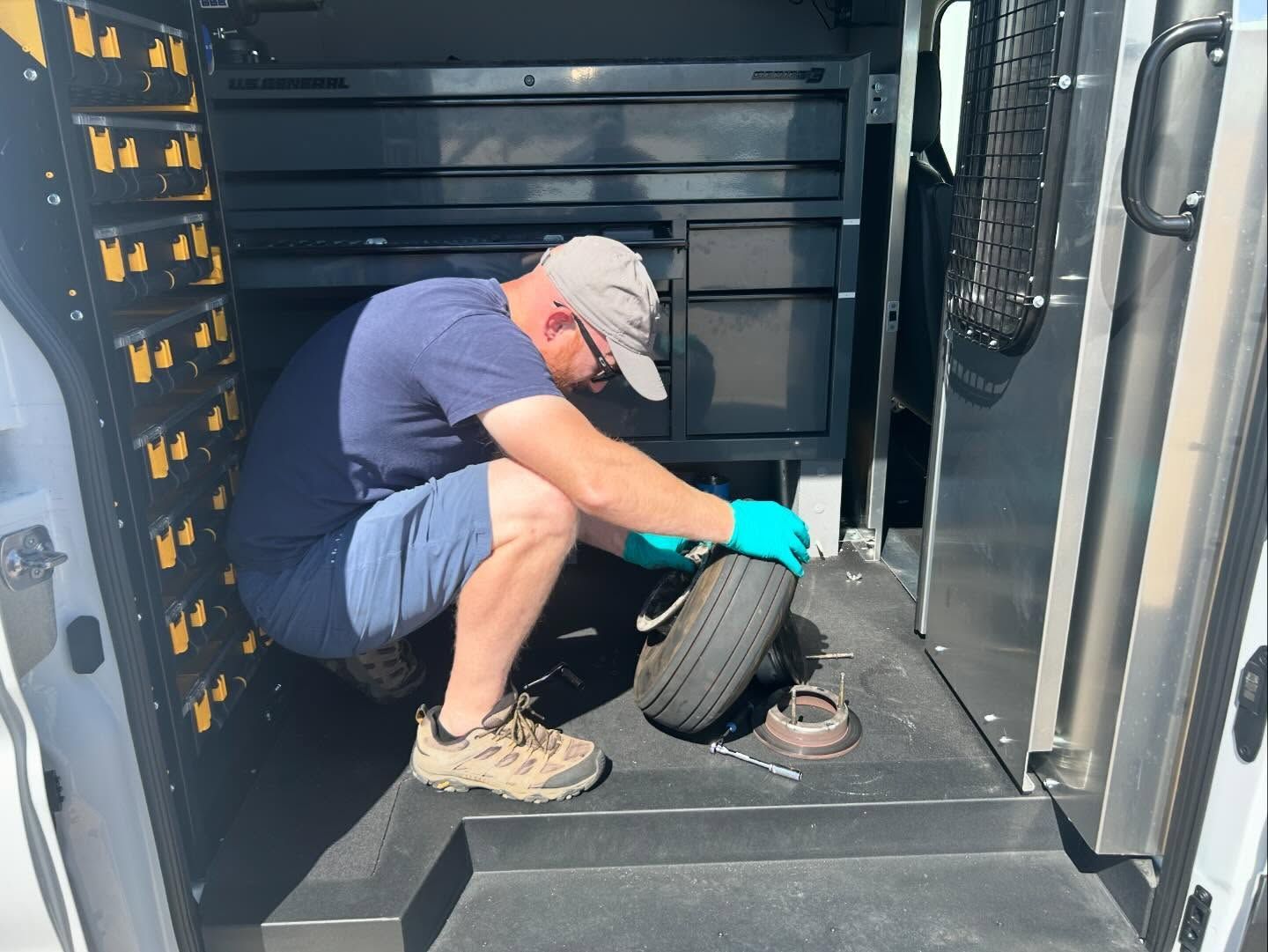 A man is kneeling down in the back of a van to change a tire.