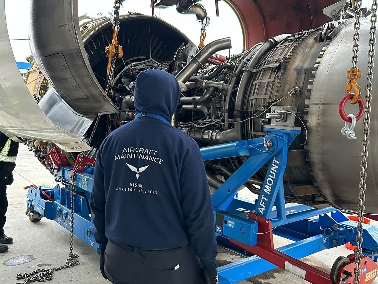 A man in a blue hoodie is standing in front of a large engine.