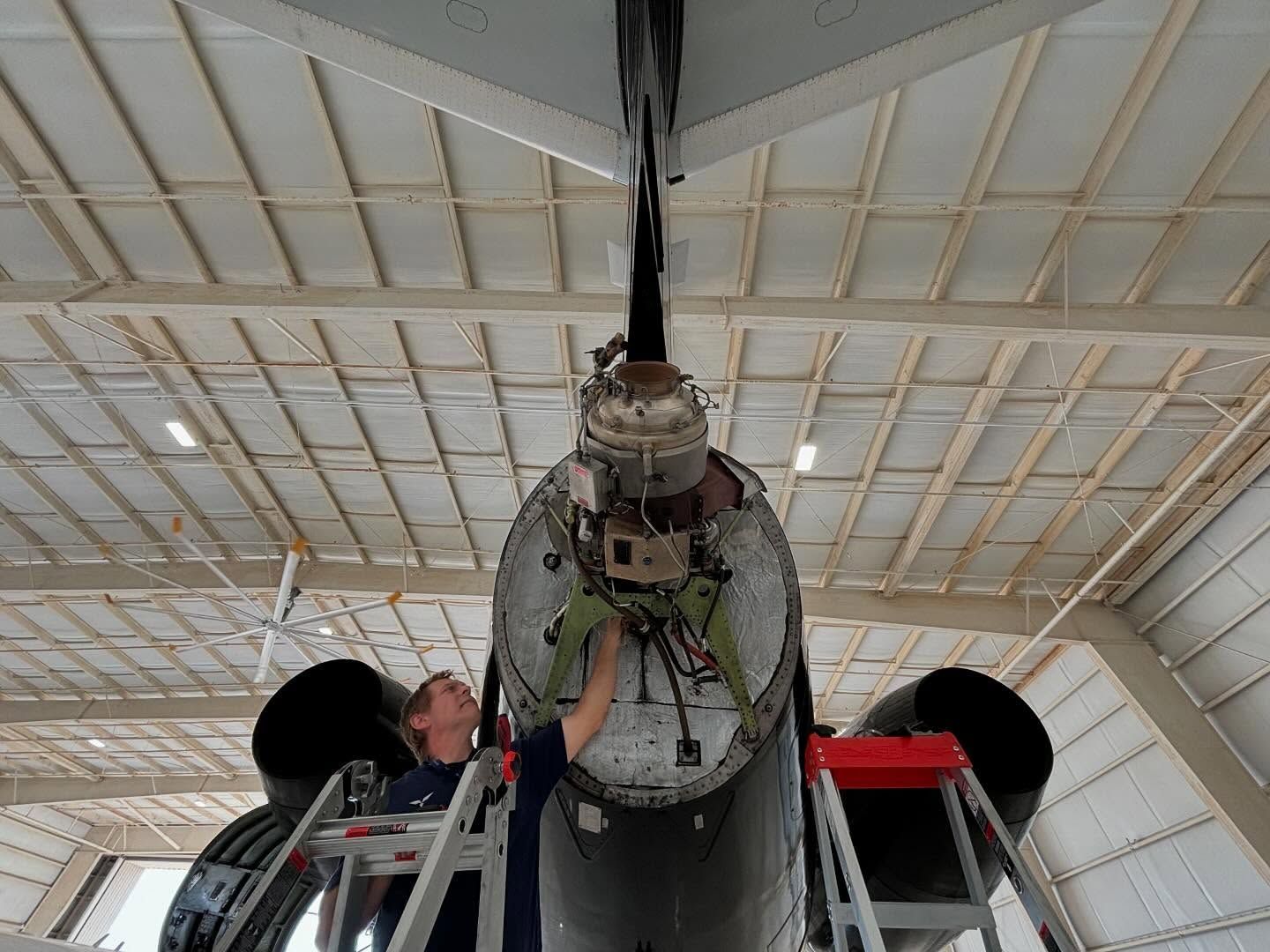 A man is working on the underside of an airplane in a hangar.