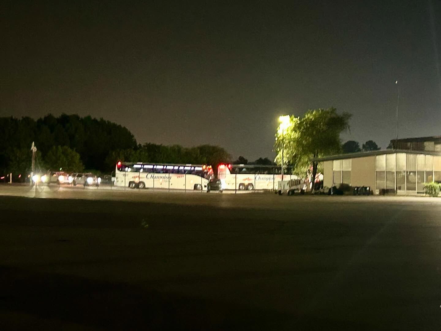A group of buses are parked in a parking lot at night.