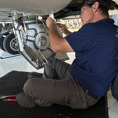 A man is kneeling down under a plane and working on it.
