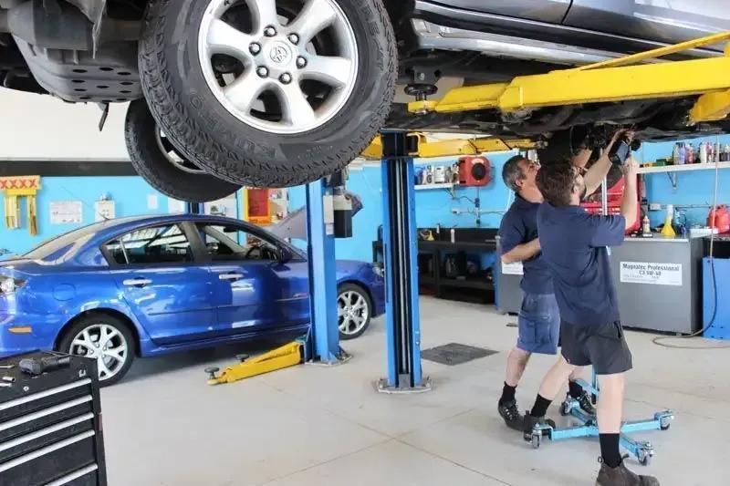 Two Men Are Working On A Blue Car On A Lift In A Garage — Currimundi Automotive Service In Warana, QLD
