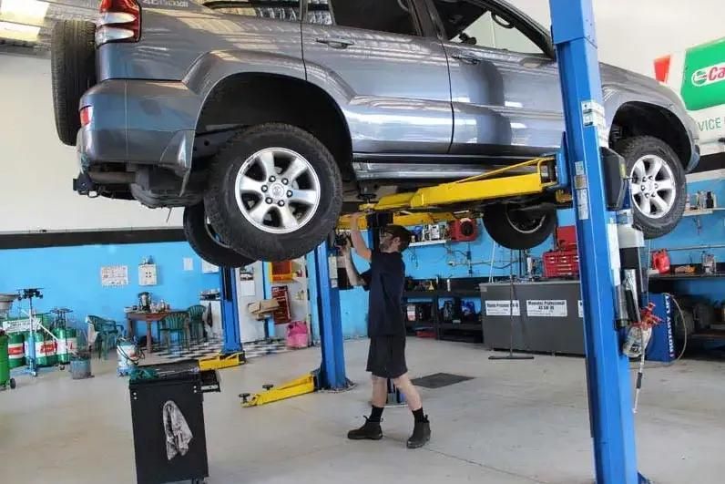 A Man Is Working On A Car On A Lift In A Garage — Currimundi Automotive Service In Warana, QLD