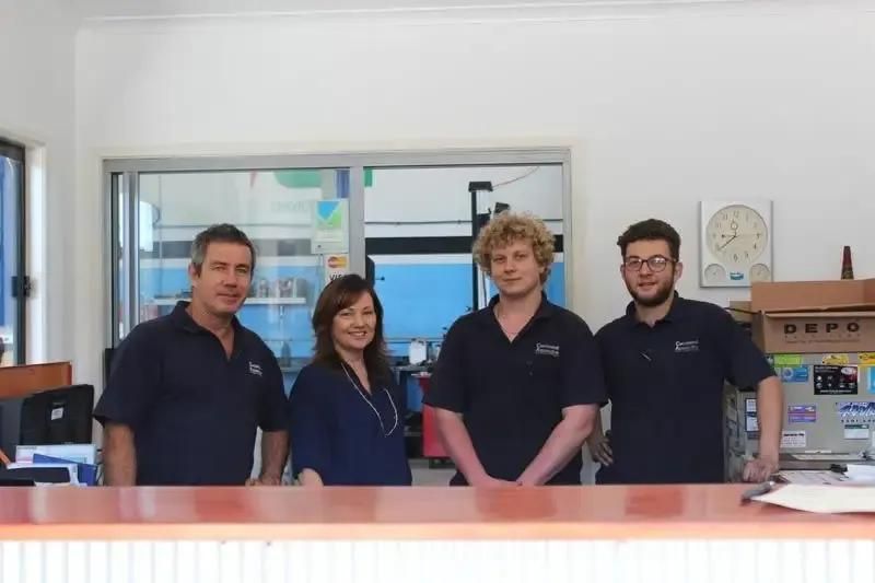 A Group Of People Are Posing For A Picture In Front Of A Counter — Currimundi Automotive Service In Warana, QLD