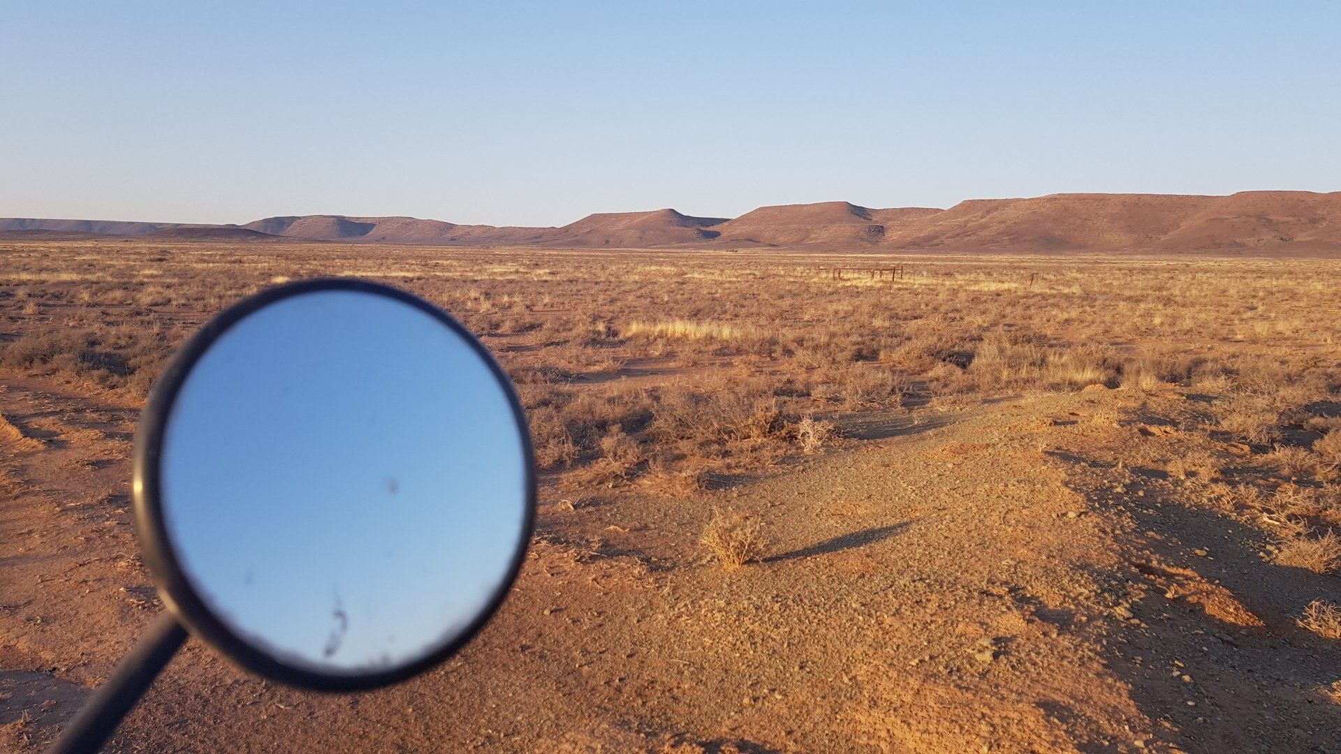 A desert landscape is reflected in a motorcycle mirror