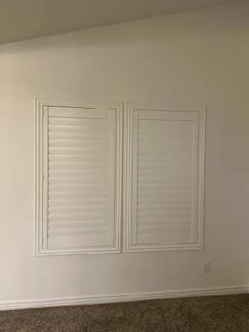 Two white shutters are hanging on a white wall in an empty room.