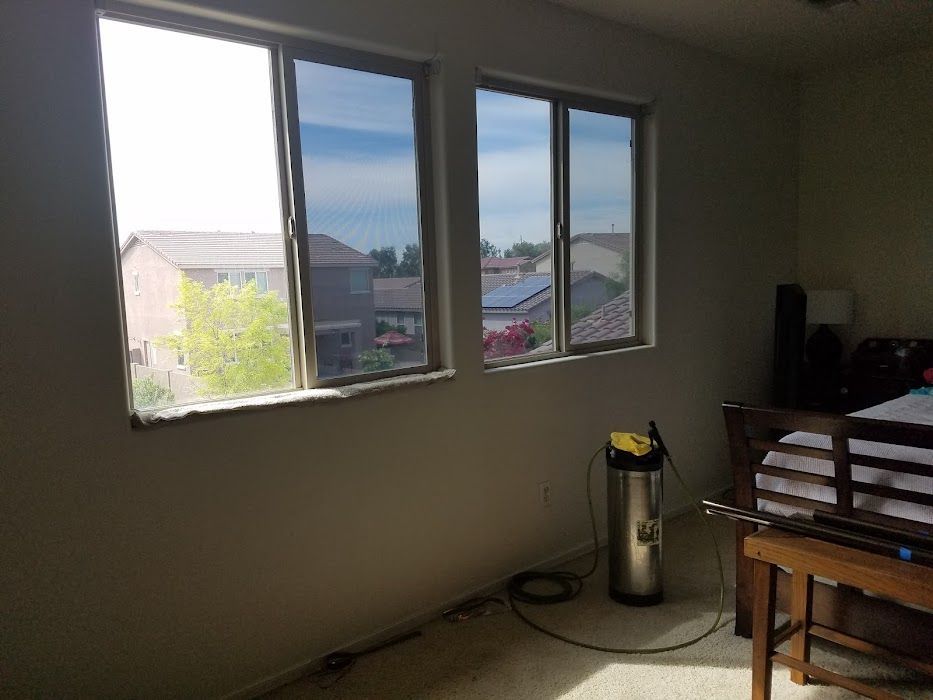 A bedroom with a bed , vacuum cleaner , and three windows.