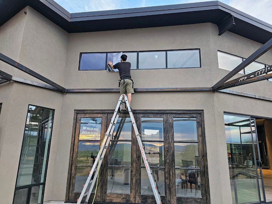 A man is standing on a ladder cleaning a window on the side of a building.