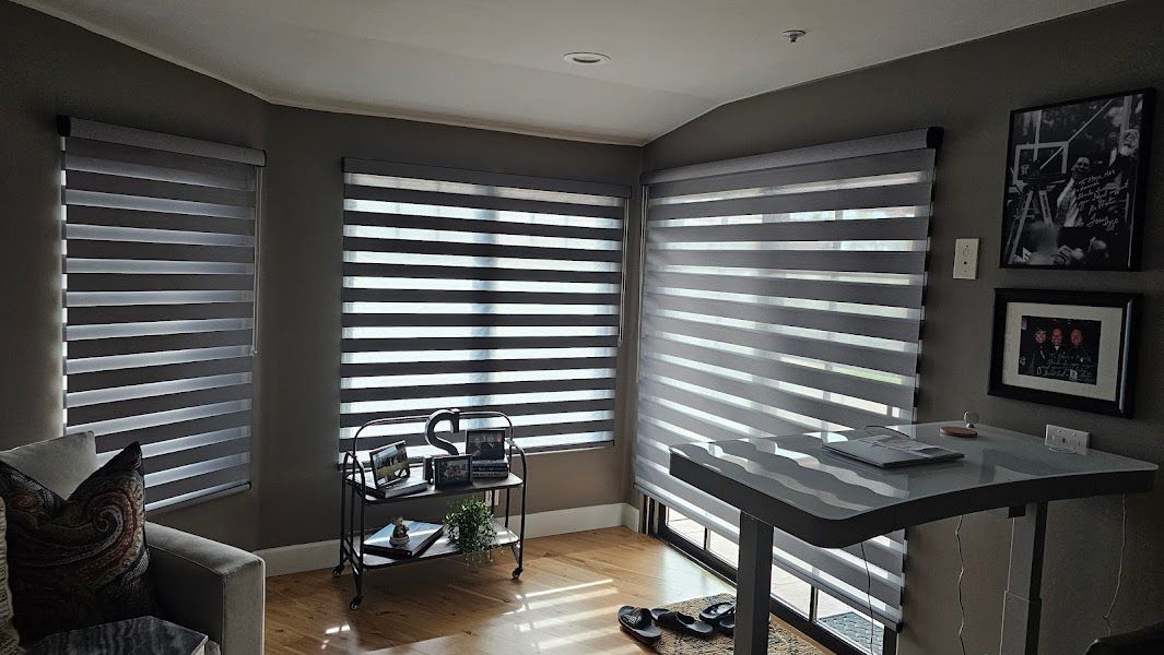 A living room with a couch , desk , and striped blinds on the windows.