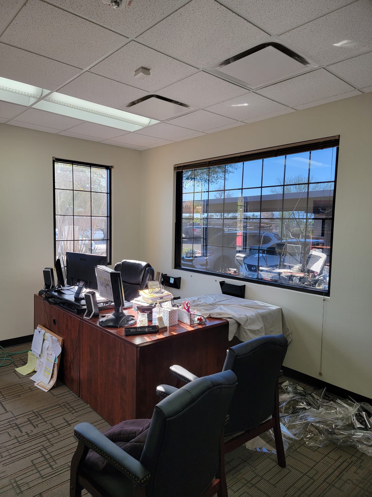 A messy office with a desk , chairs , and a window.