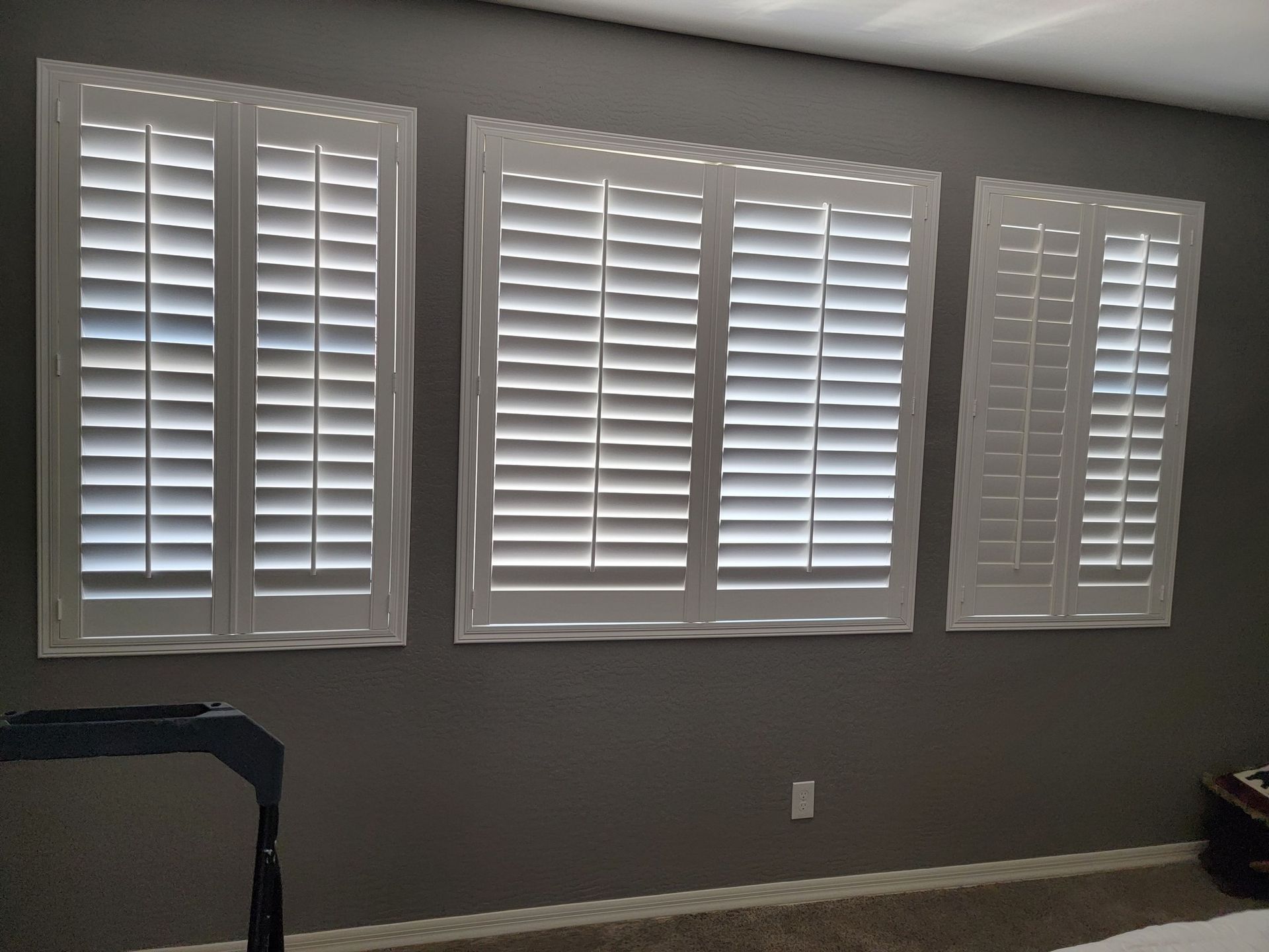 A bedroom with three windows with white shutters on them.