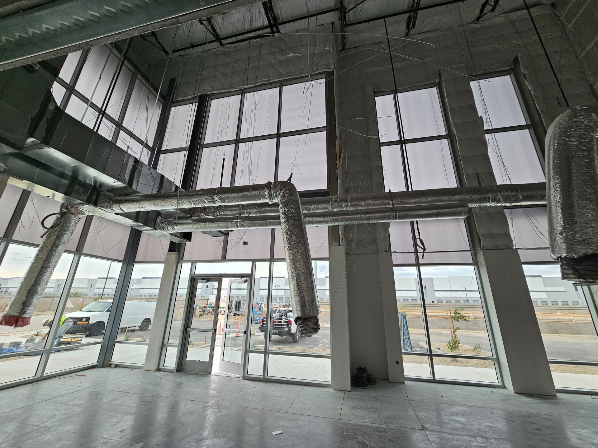 A large empty room with a lot of windows and ducts hanging from the ceiling.