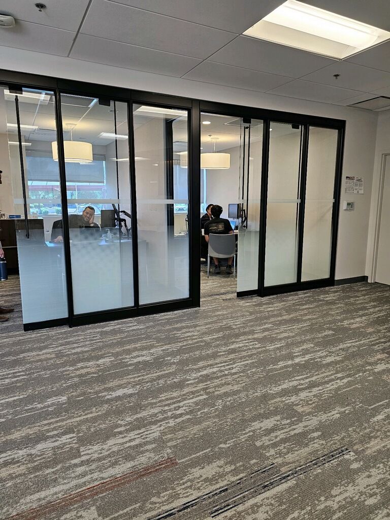 A group of people are sitting at desks in a room with sliding glass doors.