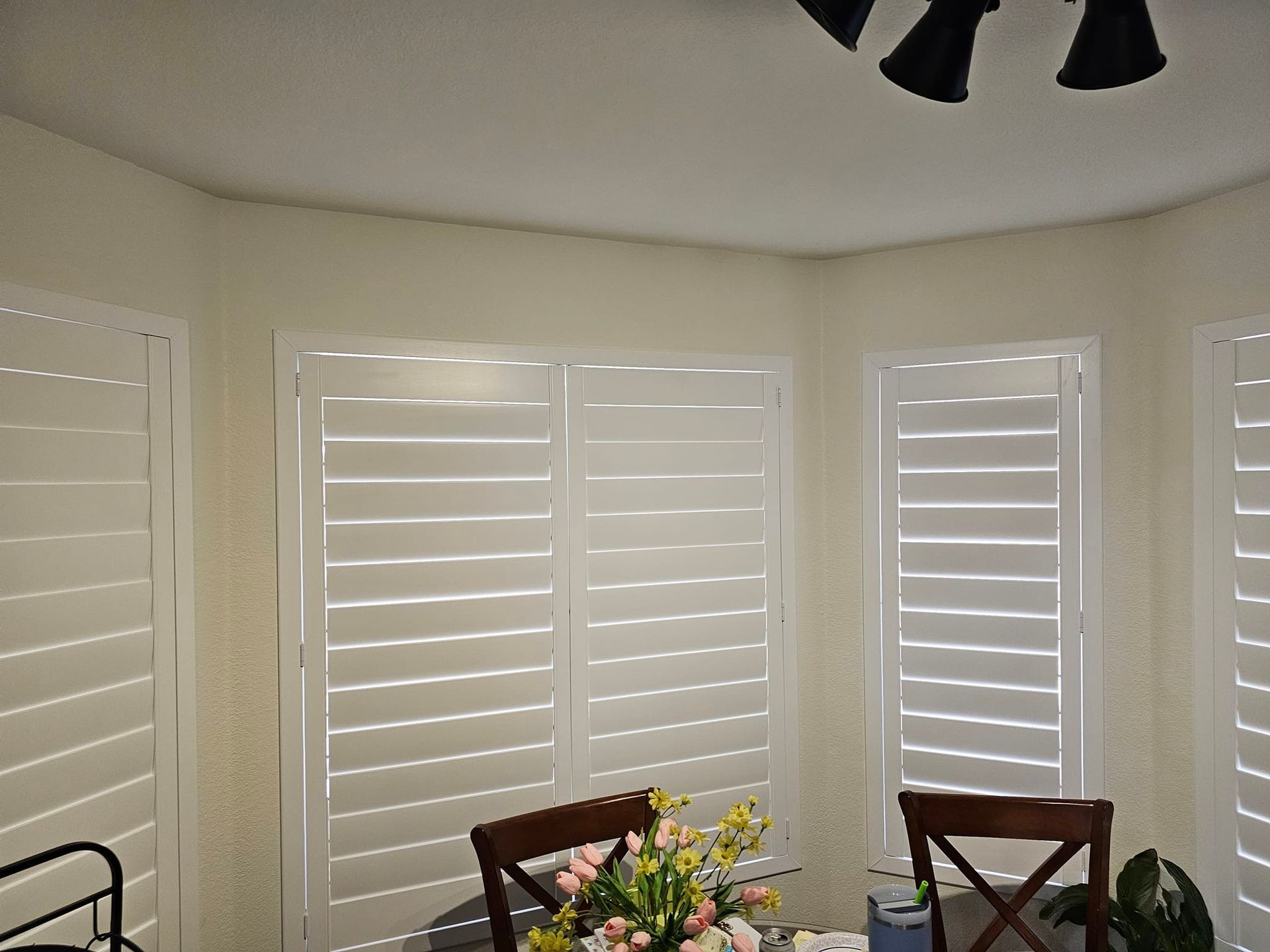 A dining room with white shutters and a ceiling fan