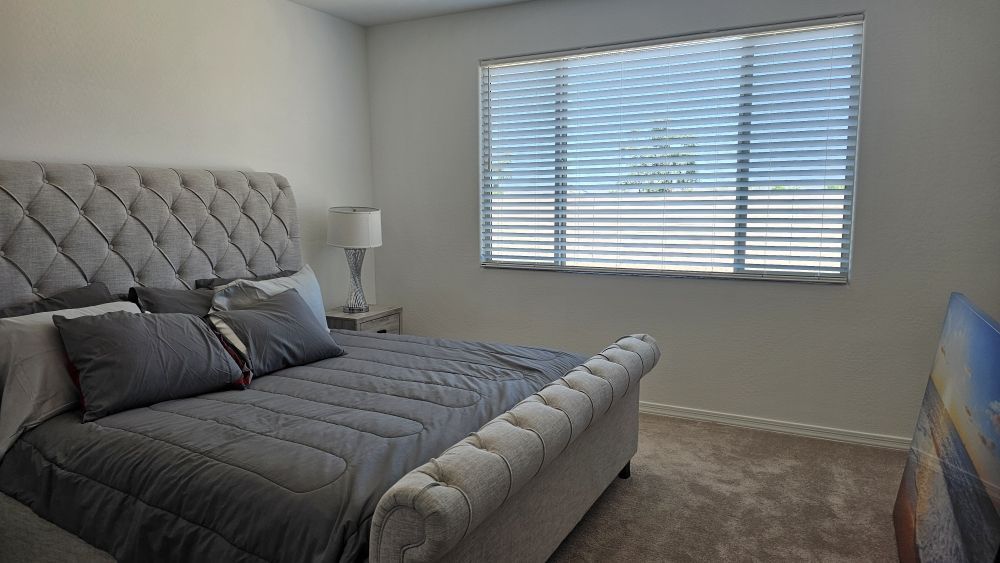 A bedroom with a large bed and a window with blinds.