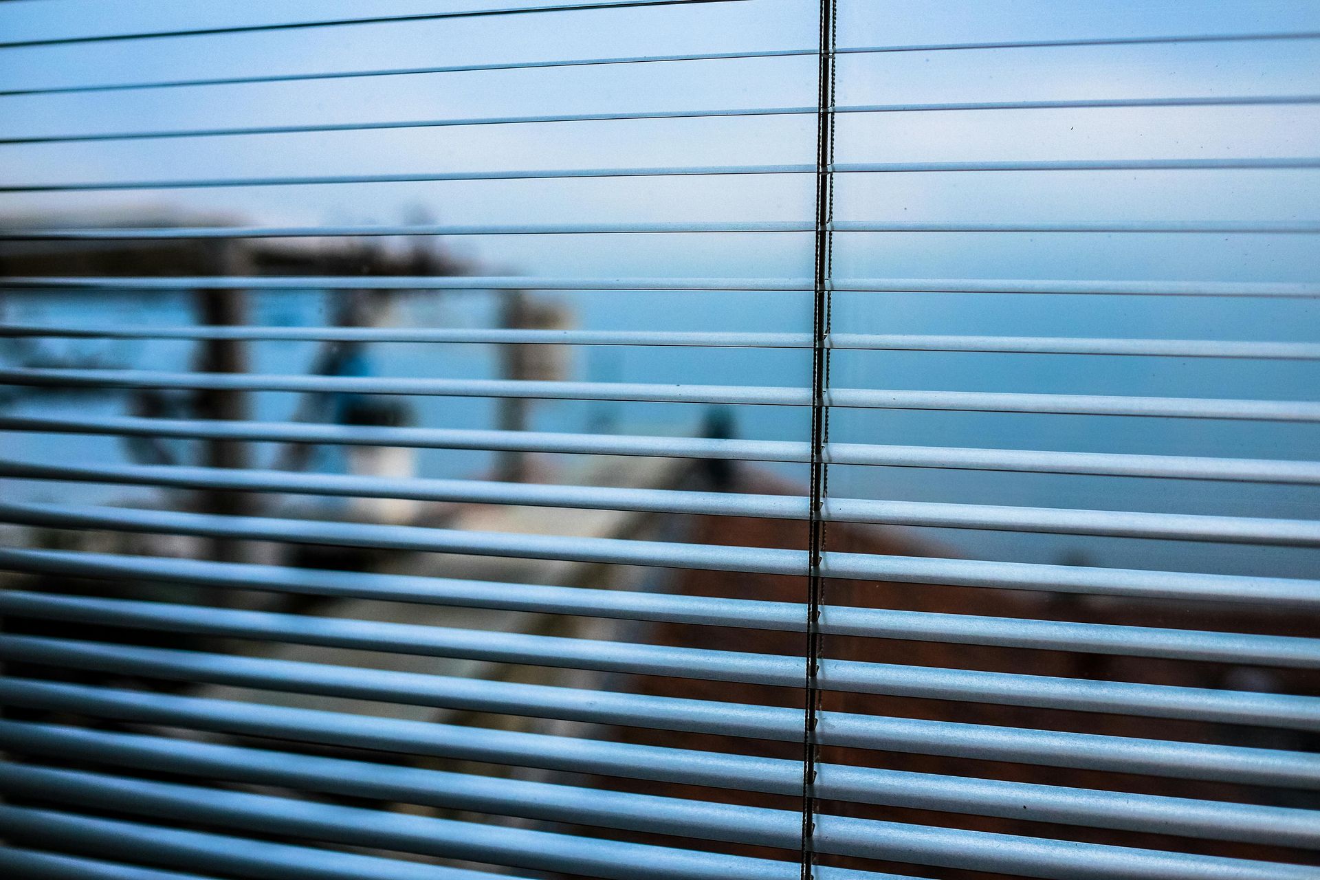 Horizontal blinds partially obscure a blurry view of a waterfront scene.