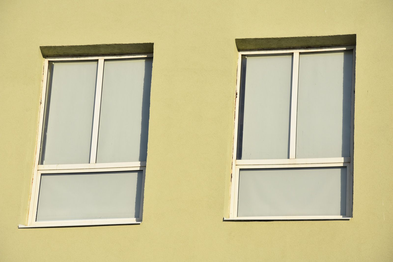 Two windows on the side of a yellow building