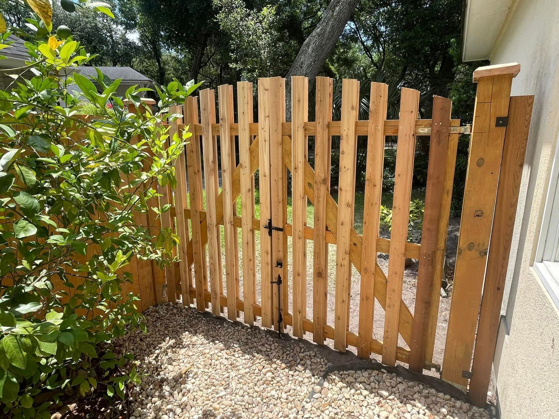 A wooden fence with a gate is surrounded by trees and gravel.
