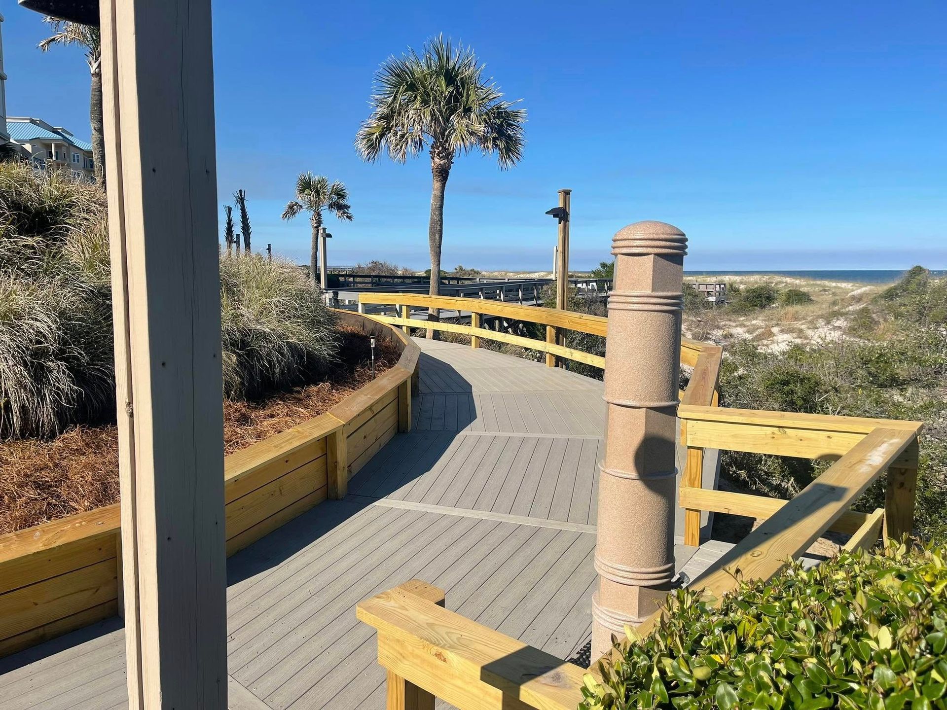 A wooden walkway leading to the beach with palm trees in the background.