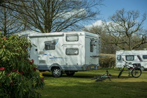 A white rv is parked in a grassy field next to a bicycle.