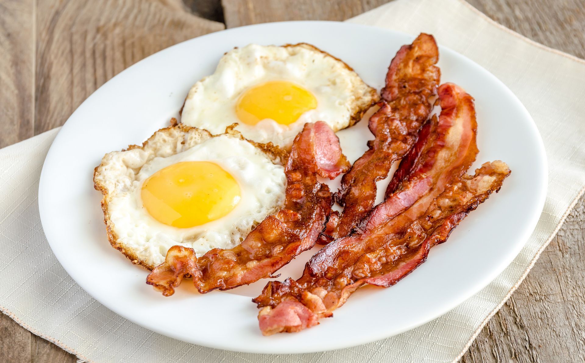A white plate topped with eggs and bacon on a table.