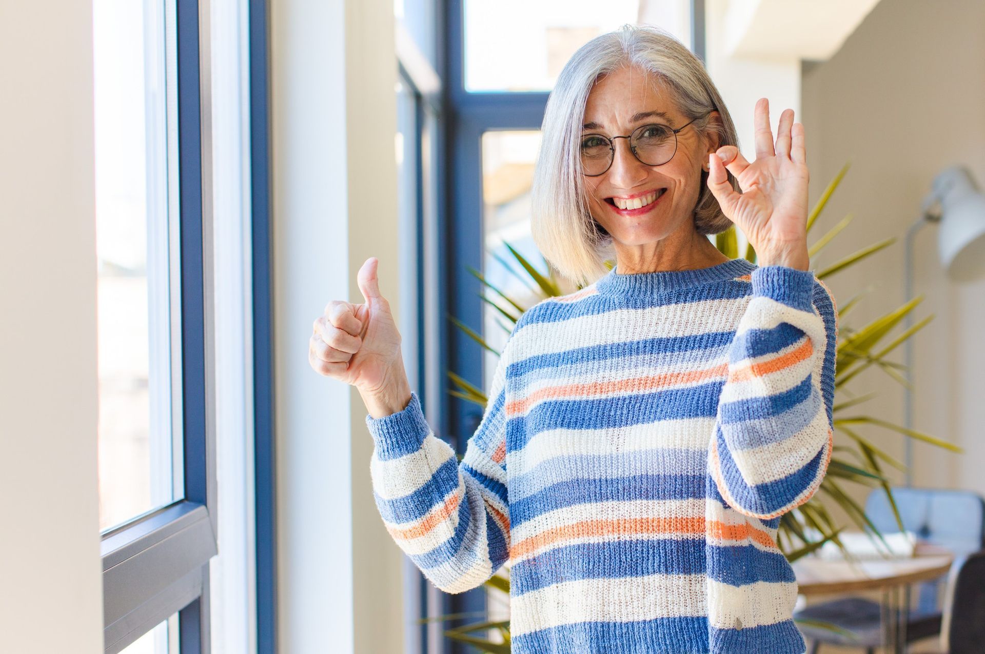 A woman in a striped sweater is giving a thumbs up sign.