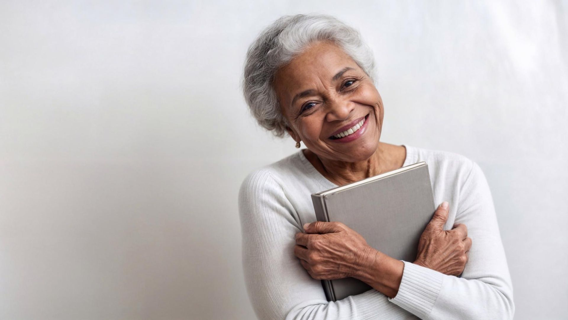 An elderly woman is hugging a book and smiling.