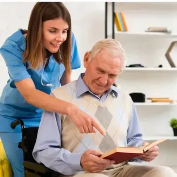 A nurse is helping an elderly man in a wheelchair read a book.