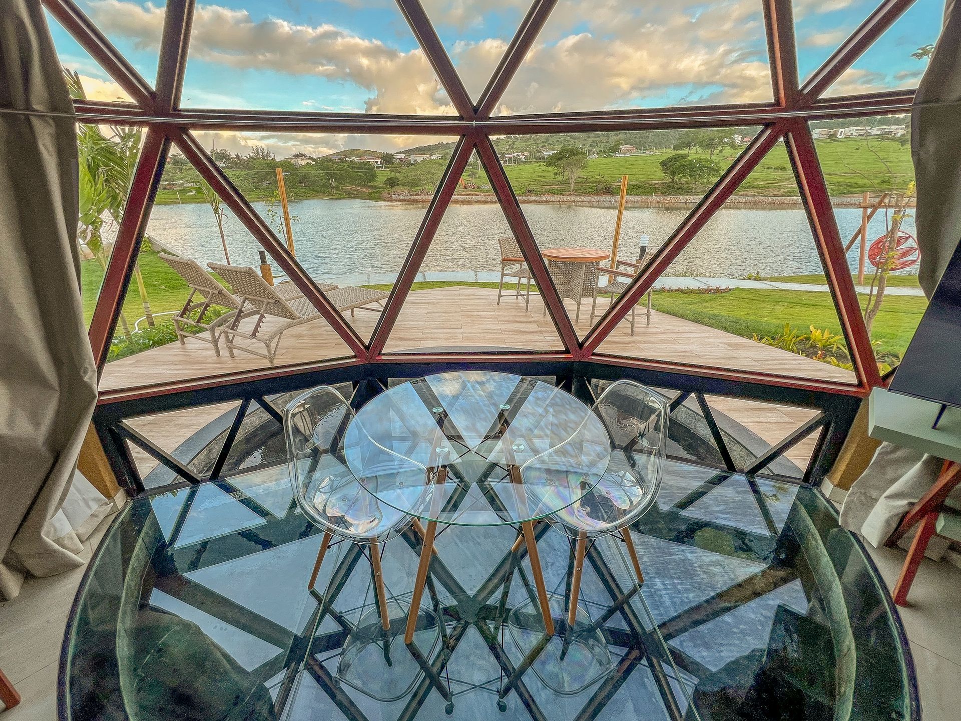Cúpula geométrica de vidro com uma mesa redonda com vista para um rio e paisagem verdejante.
