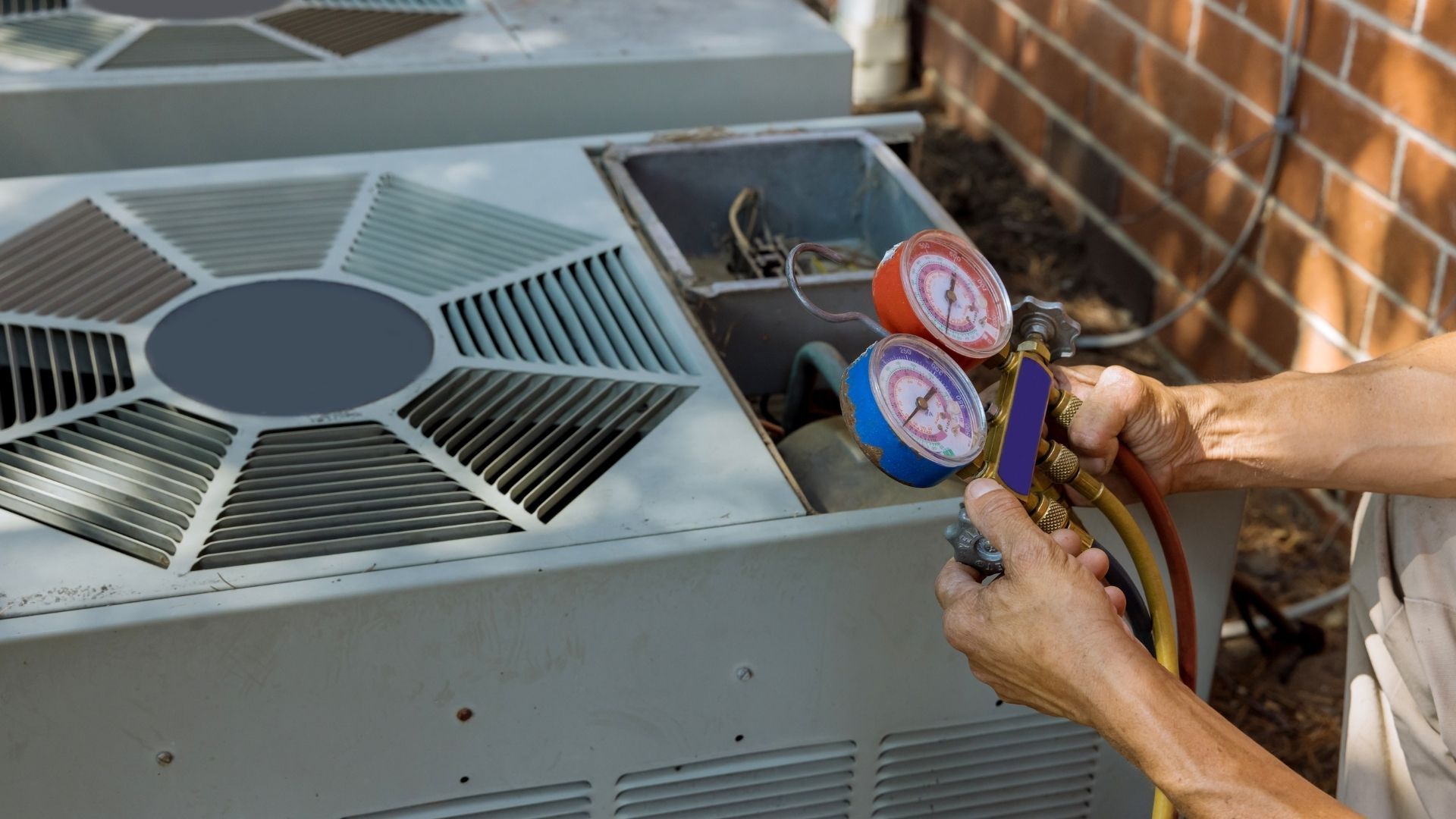A man is working on an air conditioner outside of a brick building.
