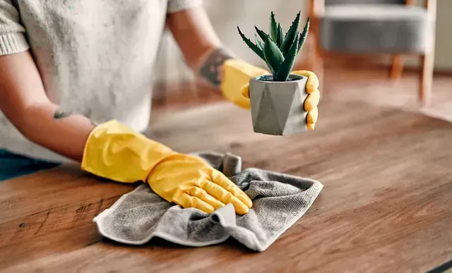 A woman wearing yellow gloves is cleaning a wooden table with a towel.