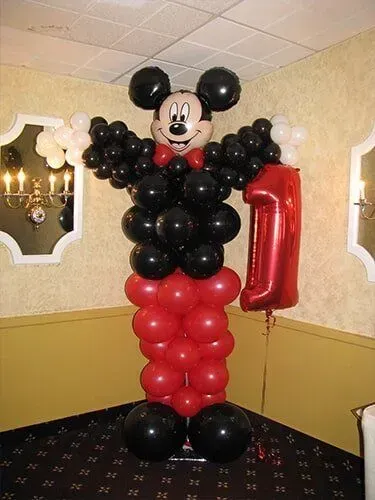 A mickey mouse made out of balloons is holding a red number one balloon.