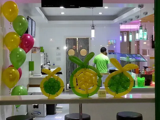 A man in a green shirt is standing behind a counter with balloons on it.