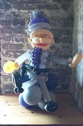 A balloon figure of a man with a mustache is sitting on a wooden table.