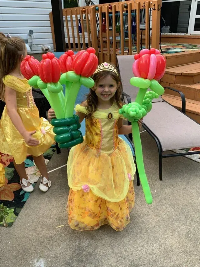 A little girl in a yellow dress is holding balloons in the shape of flowers.