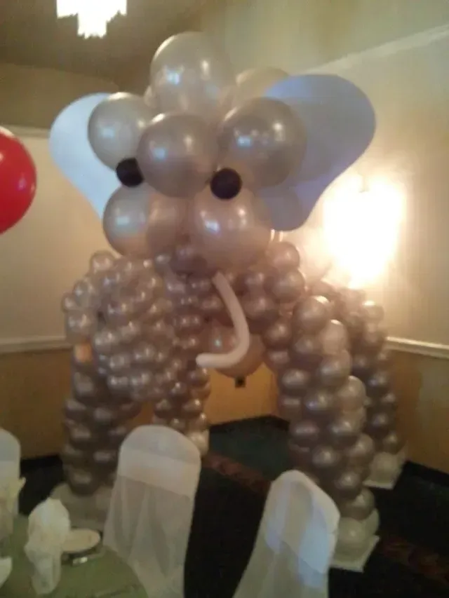An elephant made out of balloons is sitting on a table in a room.
