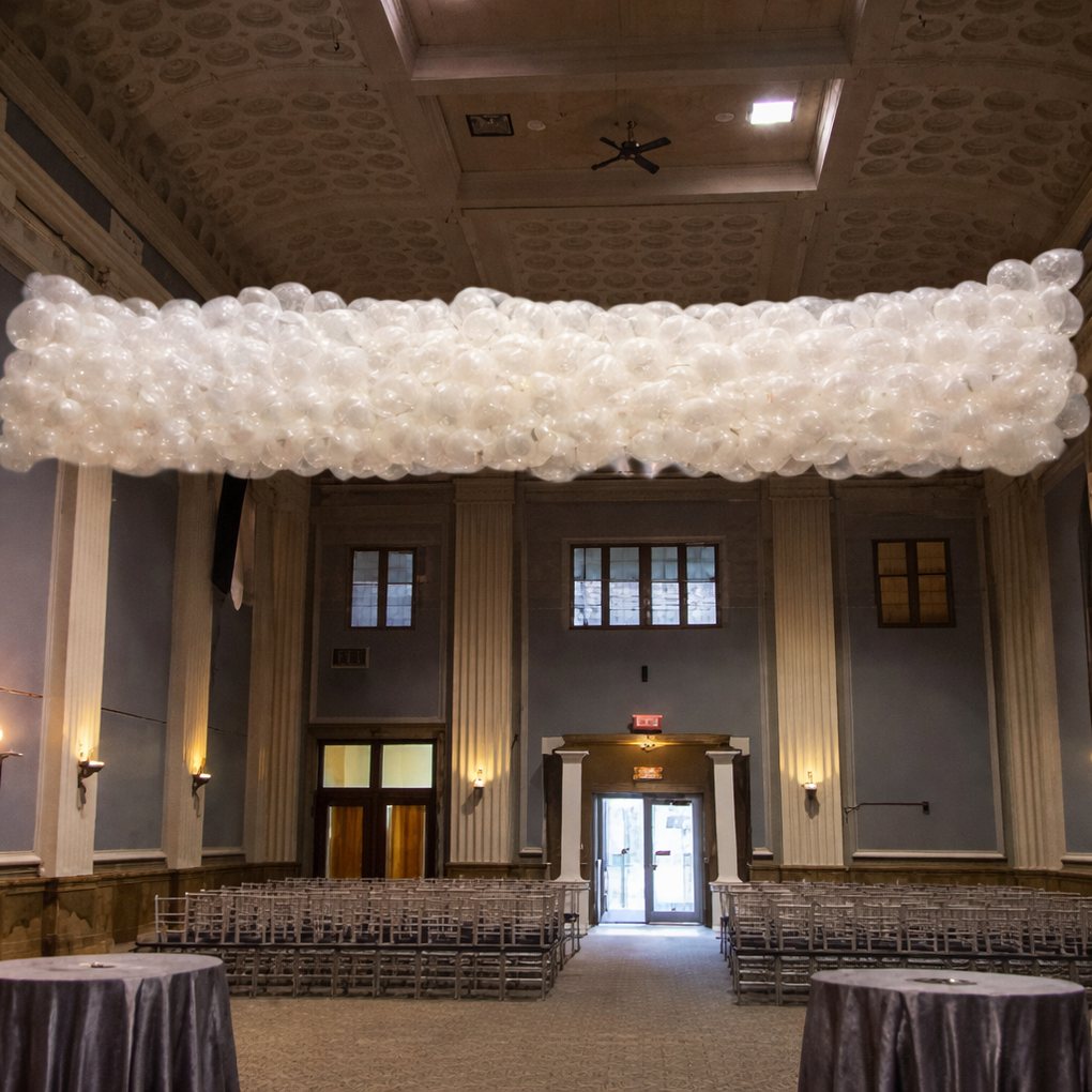 Wedding venue with rows of chairs, tables, and a large cloud of white balloons suspended from the ceiling.