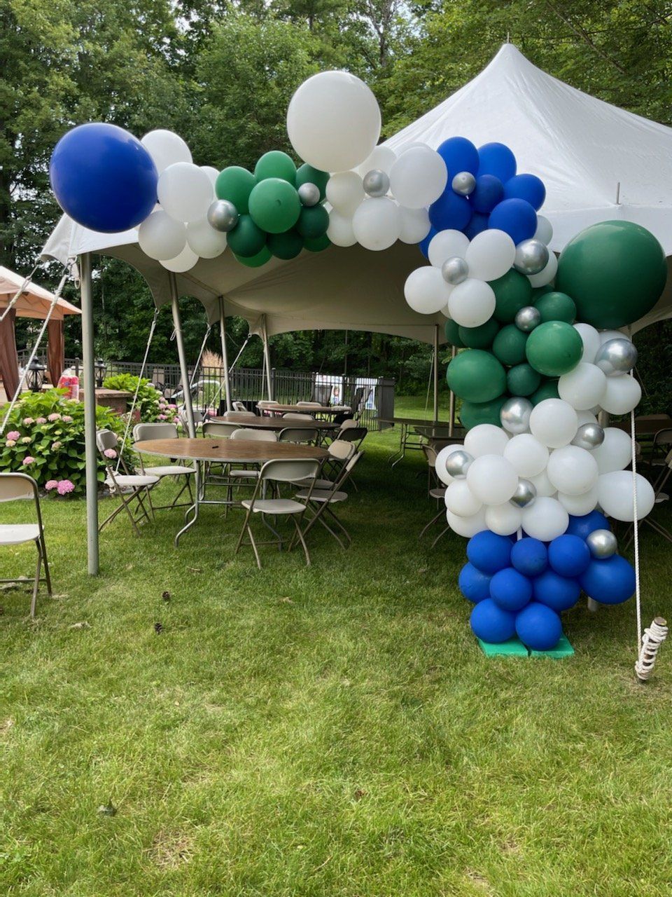 A white tent is decorated with blue , white and green balloons.