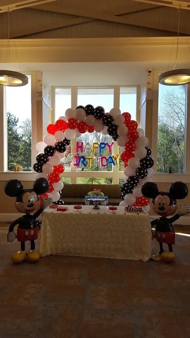 A room decorated with mickey mouse balloons and a table.