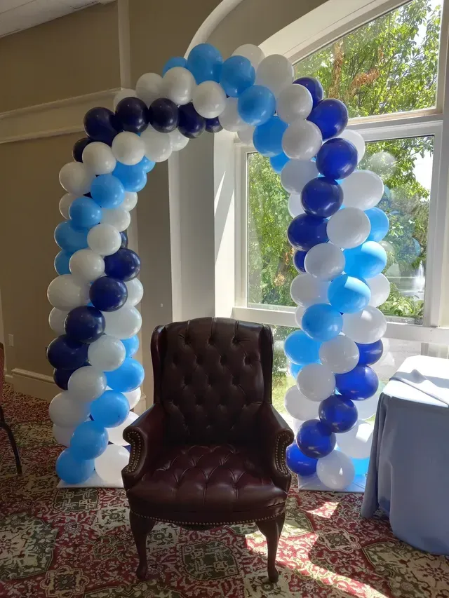 A chair is sitting under a blue and white balloon arch.
